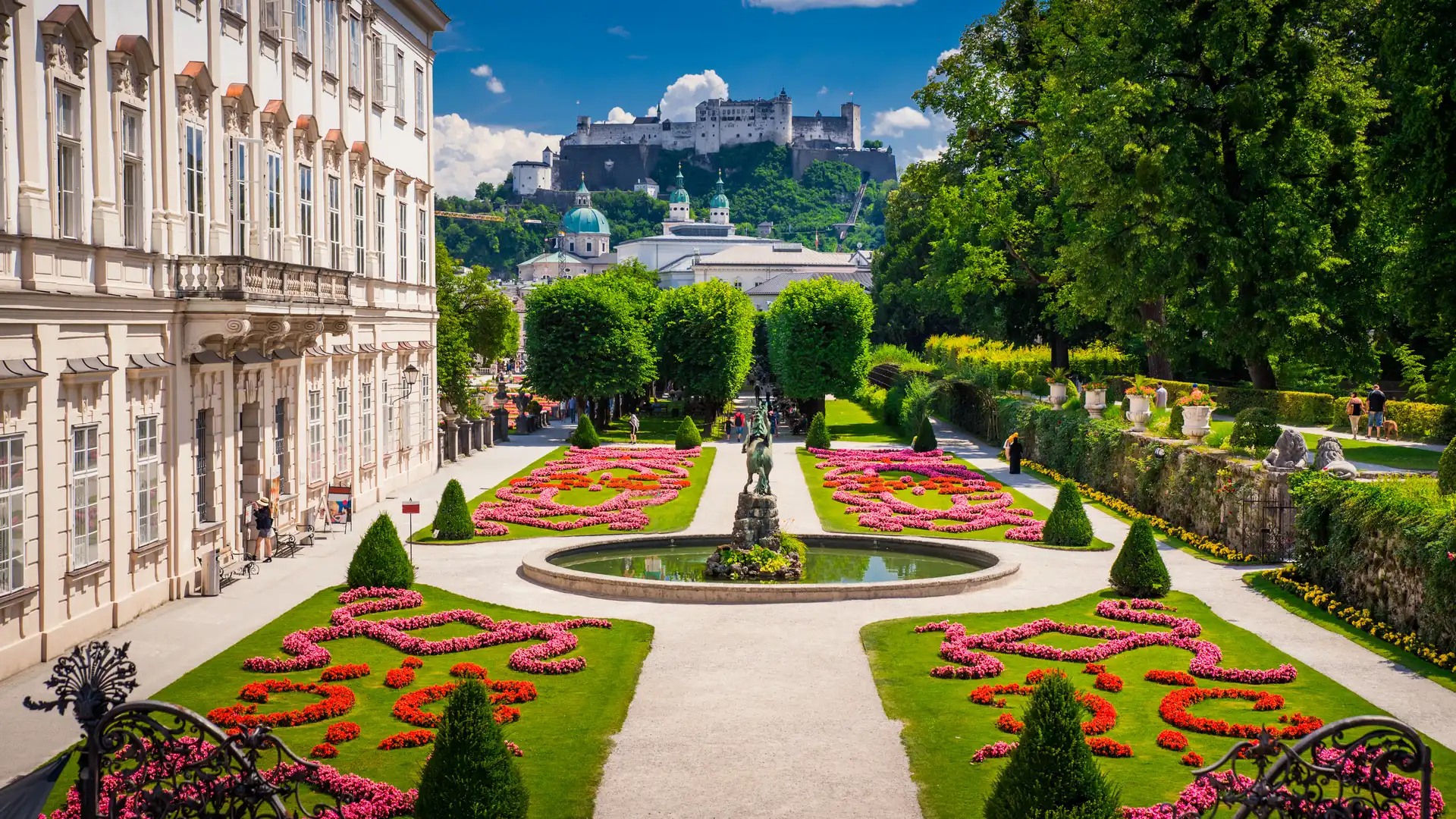 Beautiful view of Mirabell Palace Gardens in Salzburg with colorful flower arrangements and Hohensalzburg Fortress in the background
