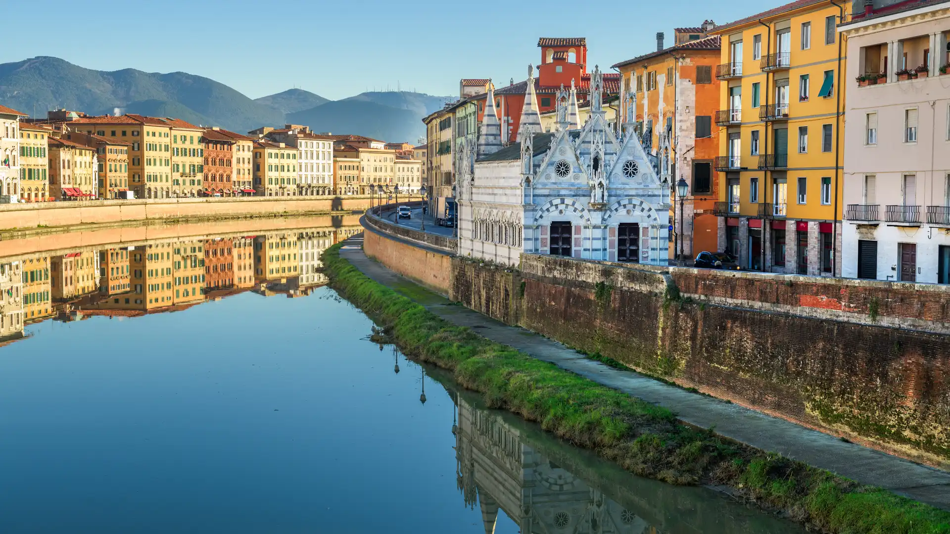 View of the Pisa river with colorful buildings and the historic architecture, reflected on the calm water.